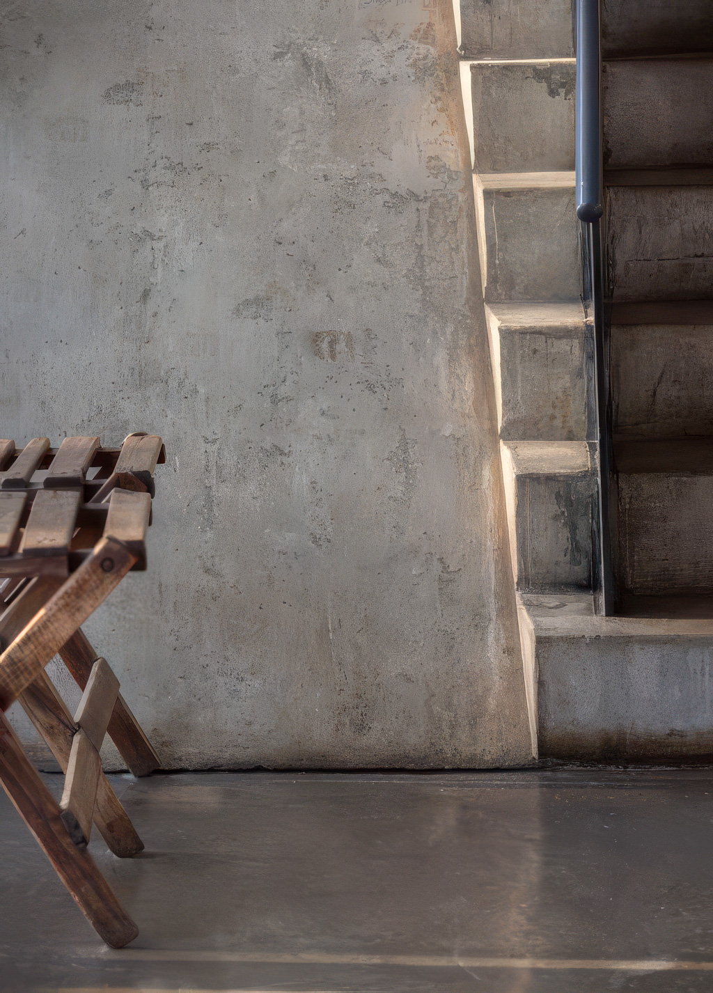 Interior detail — concrete stair, patinated wall, wooden luggage rack