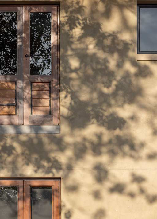 Copper-framed doors on a rendered wall, dappled with tree shadows